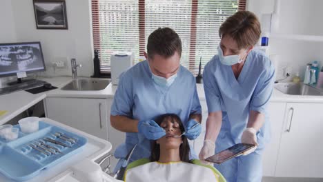 caucasian male dentist with face mask examining teeth of female patient at modern dental clinic