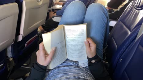 woman reading a book on an airplane and stretching across seats, air travel and tourism concept, relaxation on long distance flight