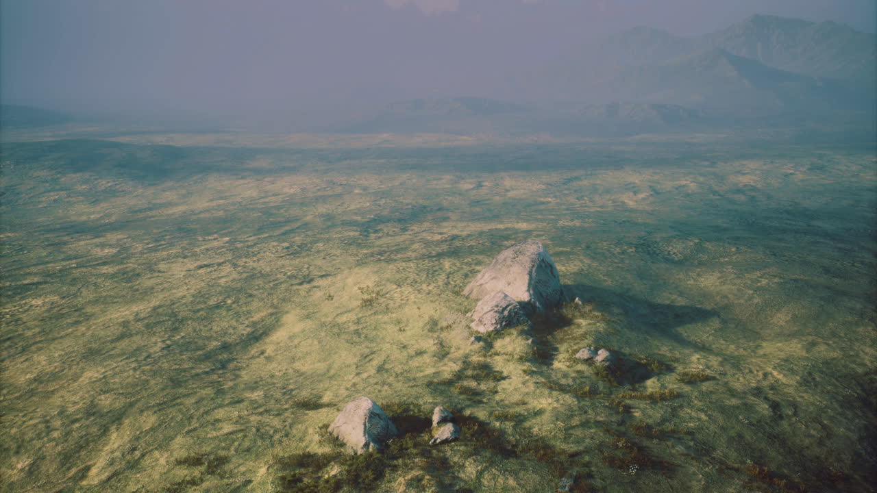 Vast landscape with large rocks and hazy mountains under soft sunlight