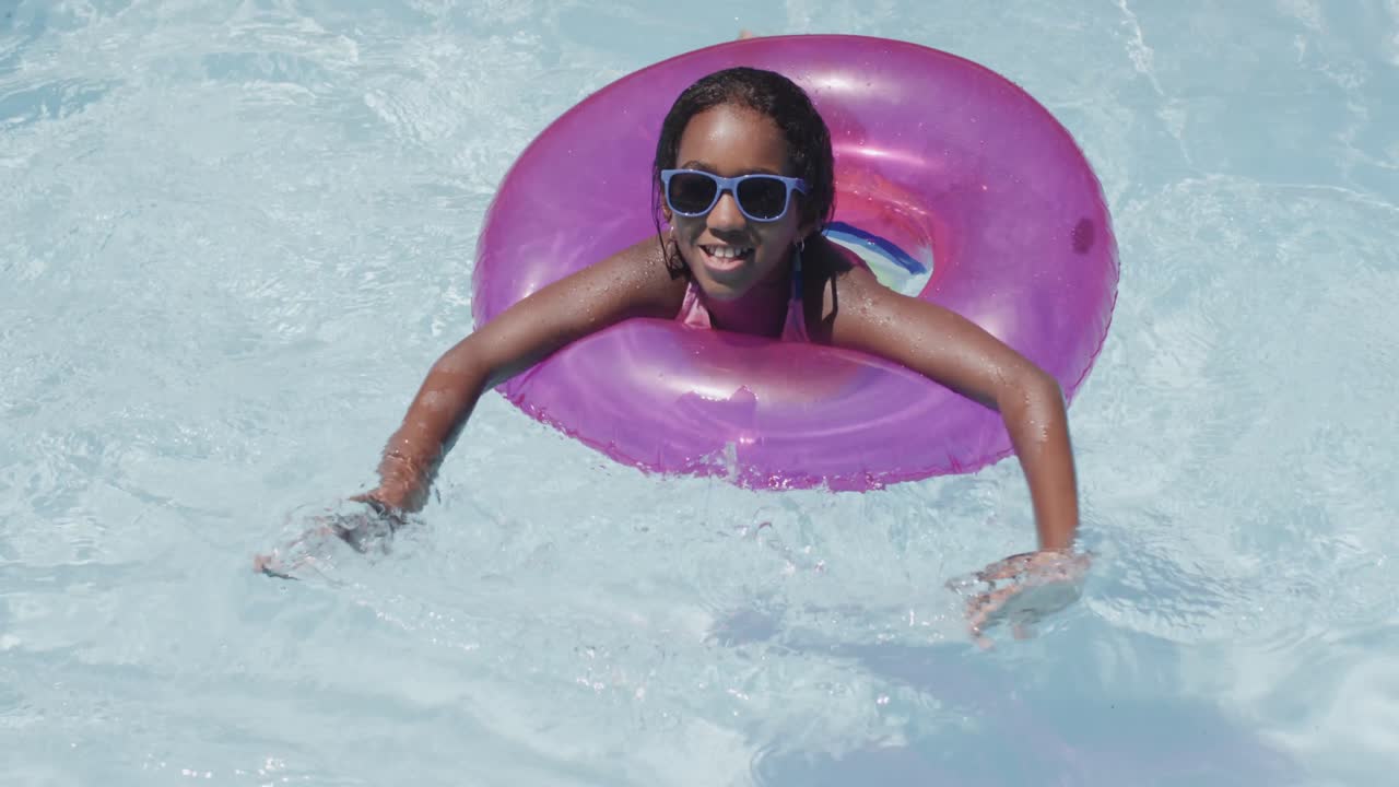 retrato de una feliz chica afroamericana usando un anillo de natación en una piscina, cámara lenta