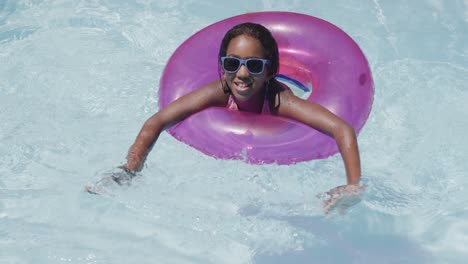 Retrato-De-Una-Feliz-Chica-Afroamericana-Usando-Un-Anillo-De-Natación-En-La-Piscina,-Cámara-Lenta