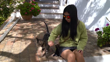 girl sitting on stairs in alley playing with stray cat