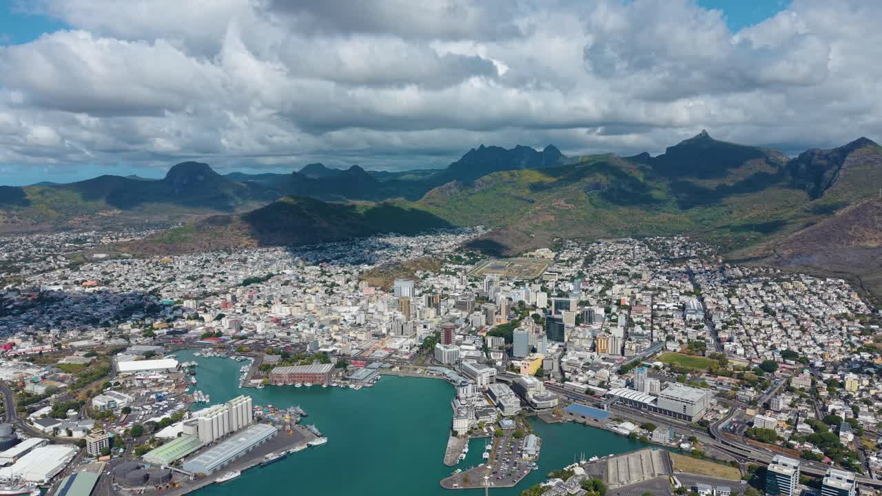 Expansive aerial view of Port Louis skyline in Mauritius. Features the bustling Caudan Waterfront, with the city nestled against the Moka Mountains and the blue ocean
