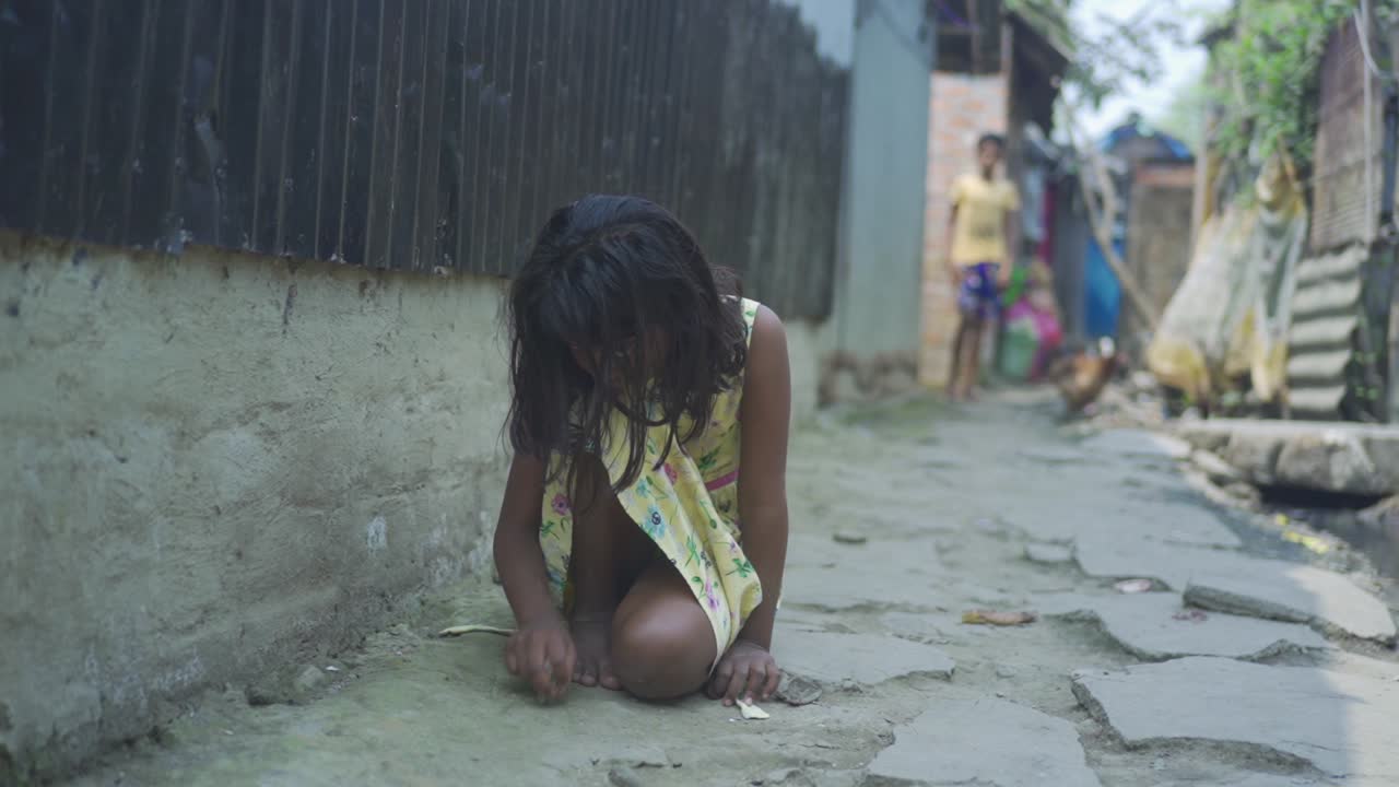 Young Indian poor orphan girl, sitting on ground playing with small rock on ground and soil, rural area