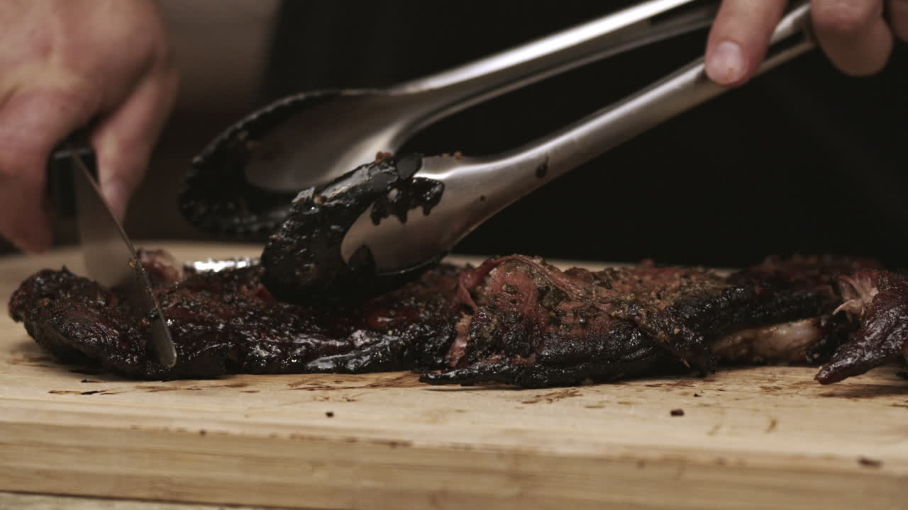 cerca de las costillas de cerdo de barbacoa siendo cortadas con un cuchillo y pinzas en la tabla de corte