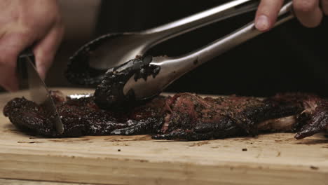 close up on bbq pork ribs being cut with a knife and tongs on cutting board