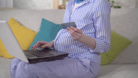 인식할 수 없는 젊은 임신한 여성이 노트북과 은행 카드를 사용합니다.
