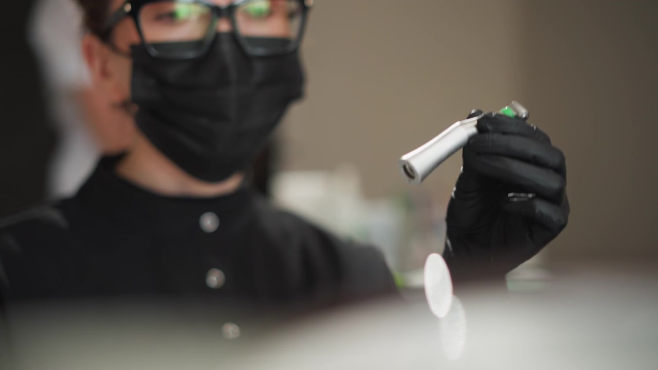 Primo piano di una persona che indossa guanti neri e occhiali, che maneggia strumenti dentali in una clinica ortodontica. La persona prepara gli strumenti per la cura del paziente, concentrandosi sulla precisione con attrezzature visibili.