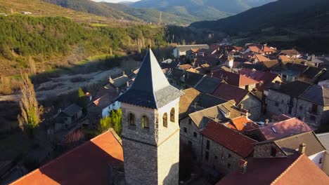 aerial video going backwards from the church and bell tower of the mountain village in aragües del puerto, surrounded by green mountains