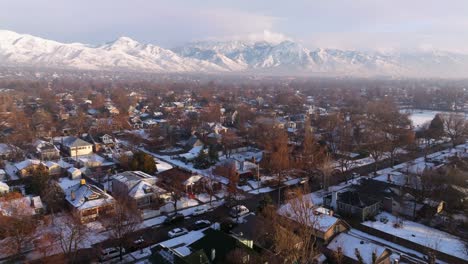 Casas-Cubiertas-De-Nieve-Iluminadas-Por-La-Luz-Del-Sol-Como-Capas-De-Niebla-Invertida-Debajo-De-Las-Impresionantes-Montañas-Wasatch-En-Invierno