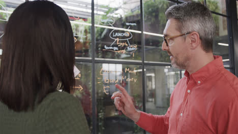 Diverse-male-and-female-colleague-brainstorming-on-glass-wall-in-office,-slow-motion