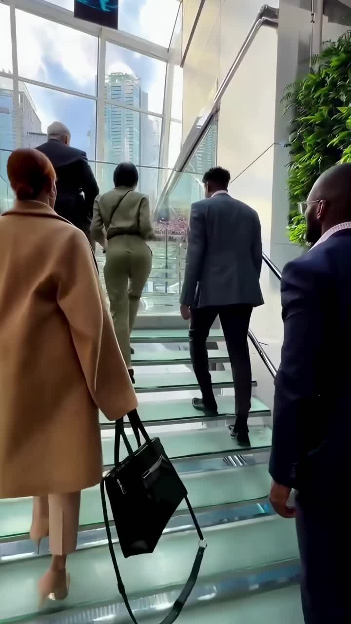 Video menampilkan sudut pandang rendah para profesional yang menaiki tangga kaca di kantor modern
