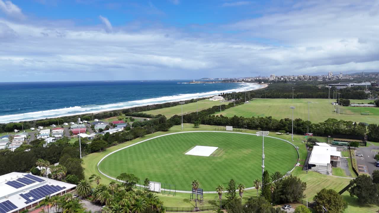 Aerial establishing orbit over Towradgi sports field and coast with ocean in background under blue skies