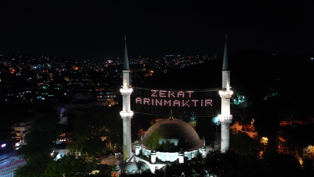 vista aérea nocturna de la mezquita de eyup sultan. dice "la limosna es purificada".