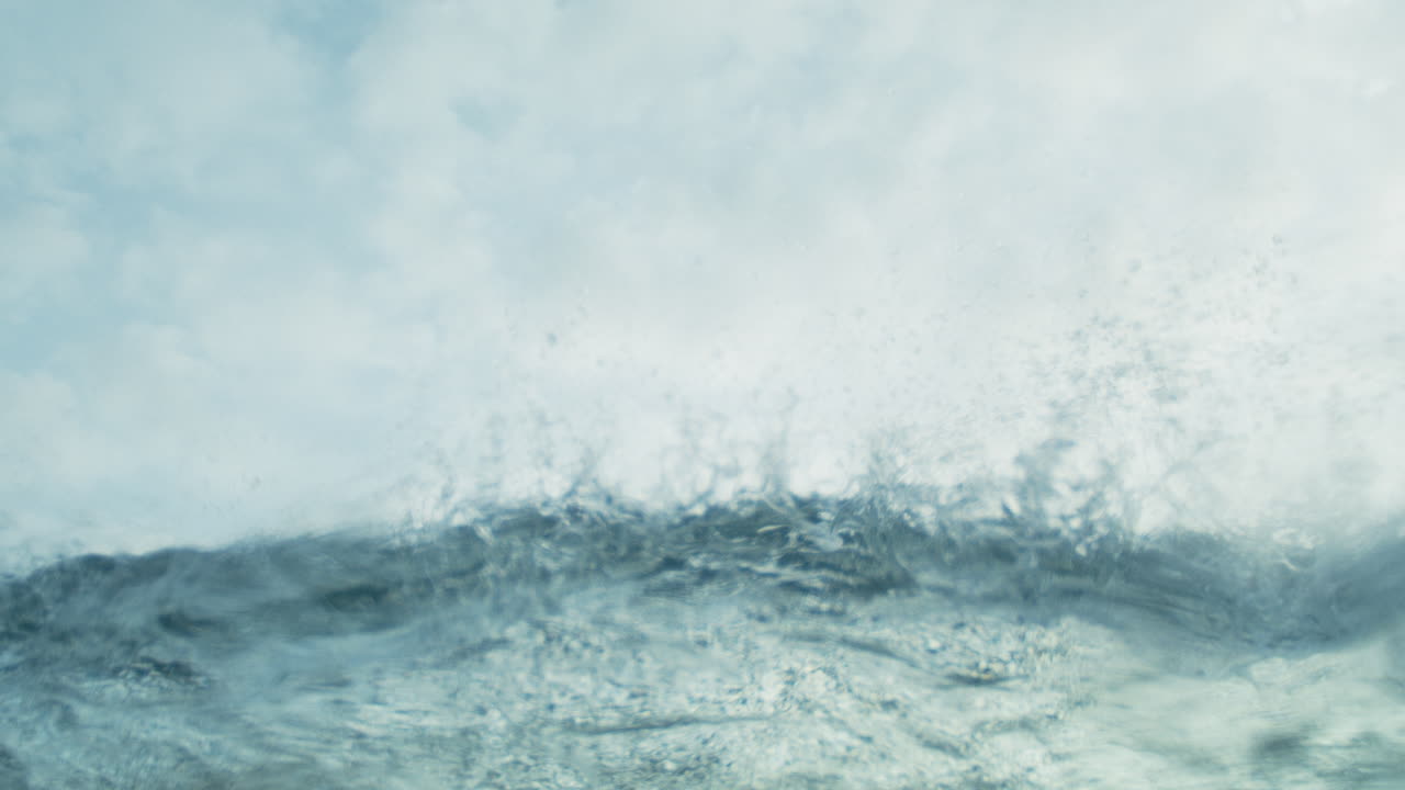 Glistening blue green wave rolls and crashes in slow motion, smooth cinematic textures