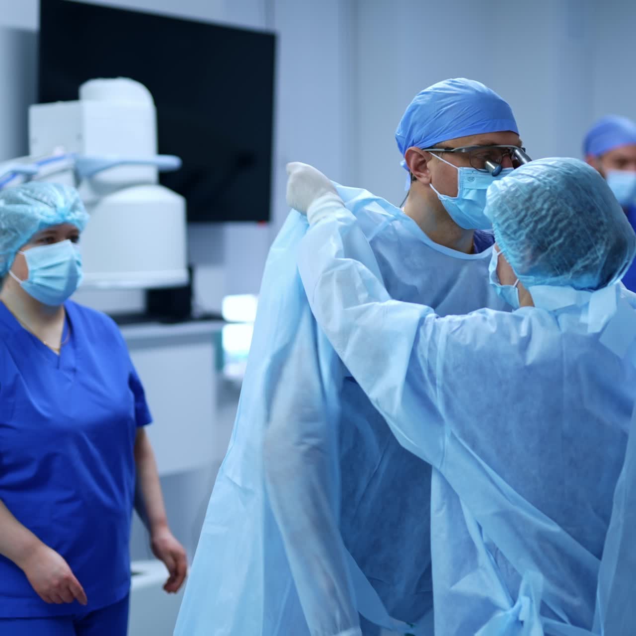 Female nurse unfolds the coat for the surgeon. Medical staff helping the doctor to put on the outfit and latex gloves