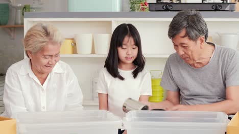 little girl and her family helping to separate plastic bottle into recyclable bin at home together.