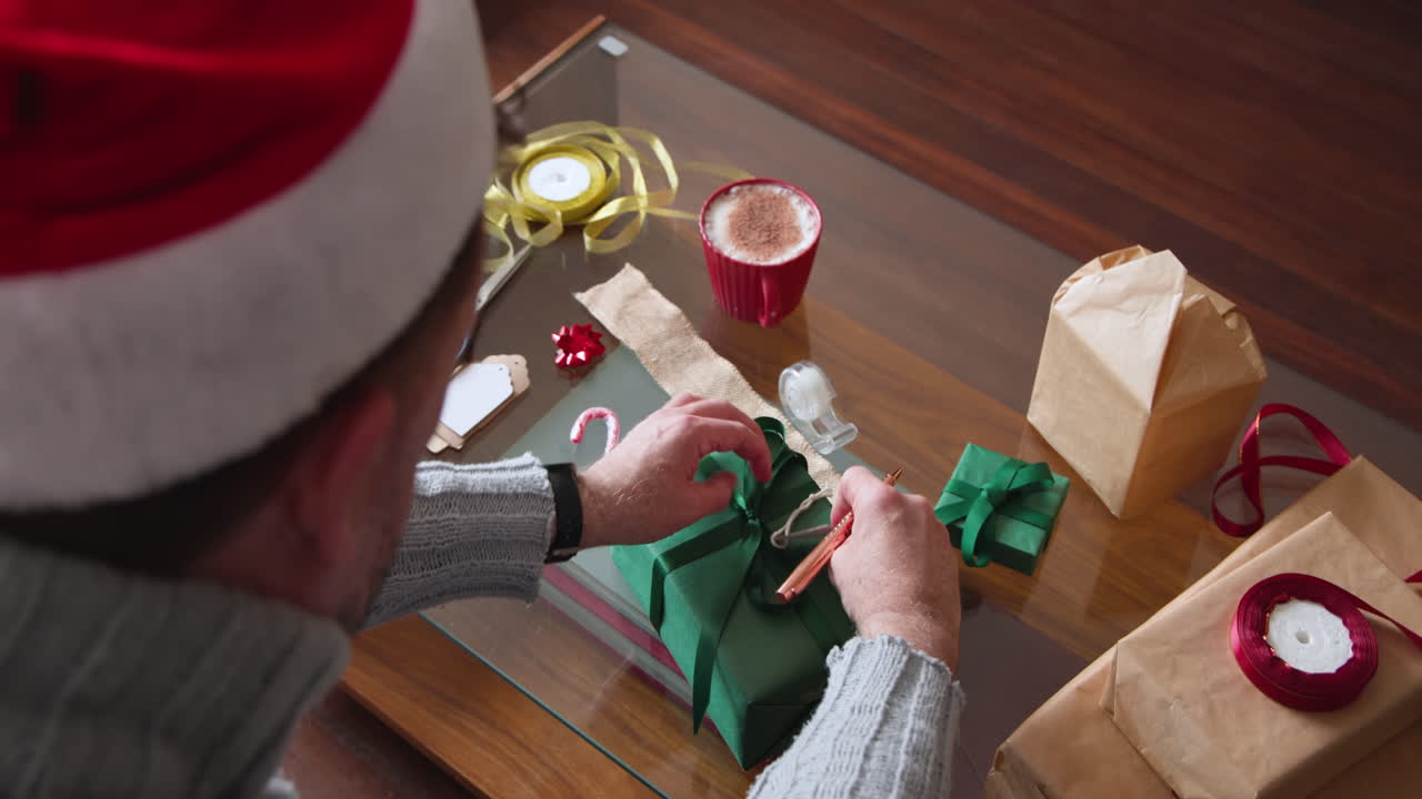 Senior man wrapping Christmas gift with ribbon and tags on wooden table