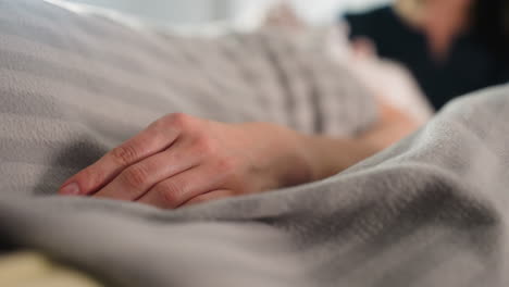 hand of recipient rests on massage bed covered with soft blanket while therapist gently massages face in blurred background, capturing serene spa treatment ambiance and client relaxation