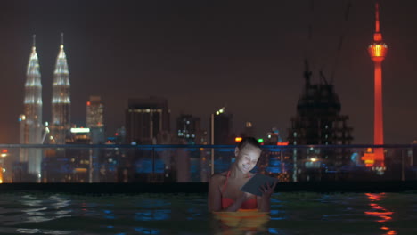 woman with pad in rooftop pool of night kuala lumpur