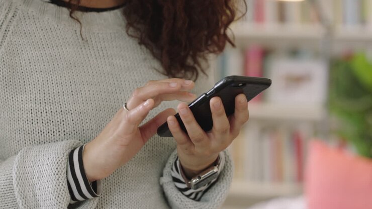 vicino le mani di una giovane donna che usa lo smartphone, che manda sms, che naviga, che comunica con il cellulare, che si connette online.
