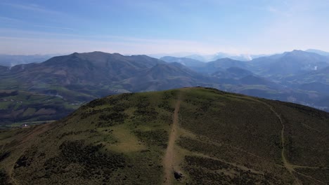 Mountain-top-in-the-Pyrénées-Atlantiques-French-Basque-Country-with-green-and-brown-rolling-hills-and-snow-capped-mountains-in-the-background