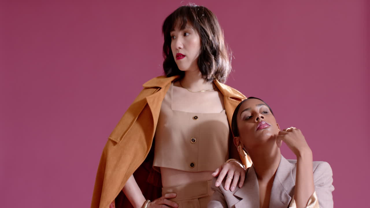 Diverse female models stepping into frame creating twin model poses on pink chair in studio