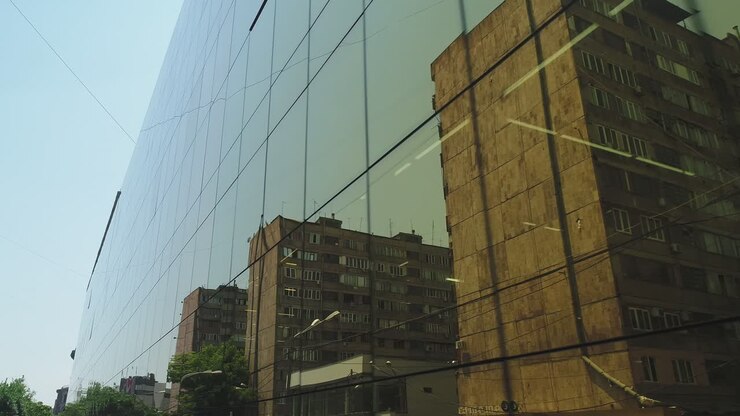 Vista esterna 4K di giorno di un edificio di un quartiere degli affari o di un centro commerciale con finestre a specchio. Luce solare. Riflesso di città, auto e torri nelle pareti a specchio. Movimento della telecamera drone.