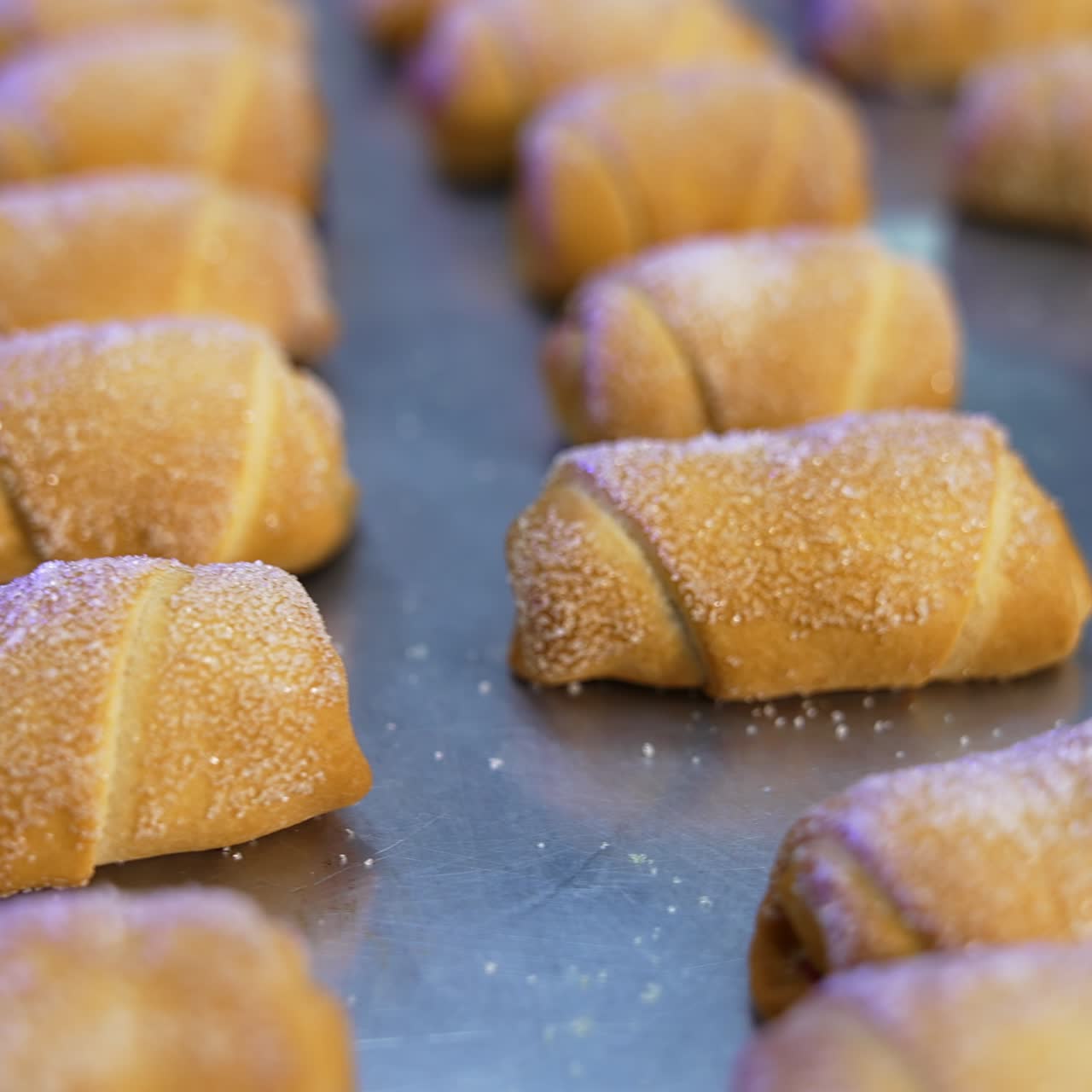 Savory delicious little croissants sprinkled with sugar at baking sheet. Tray full of desserts on a turning table. Close up
