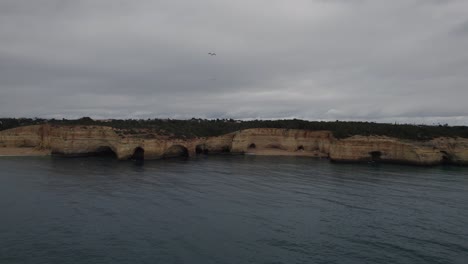 Aerial-view-push-in-towards-Benagil-caves,-Algarve-Portugal-with-Atlantic-ocean-transparent-coastline