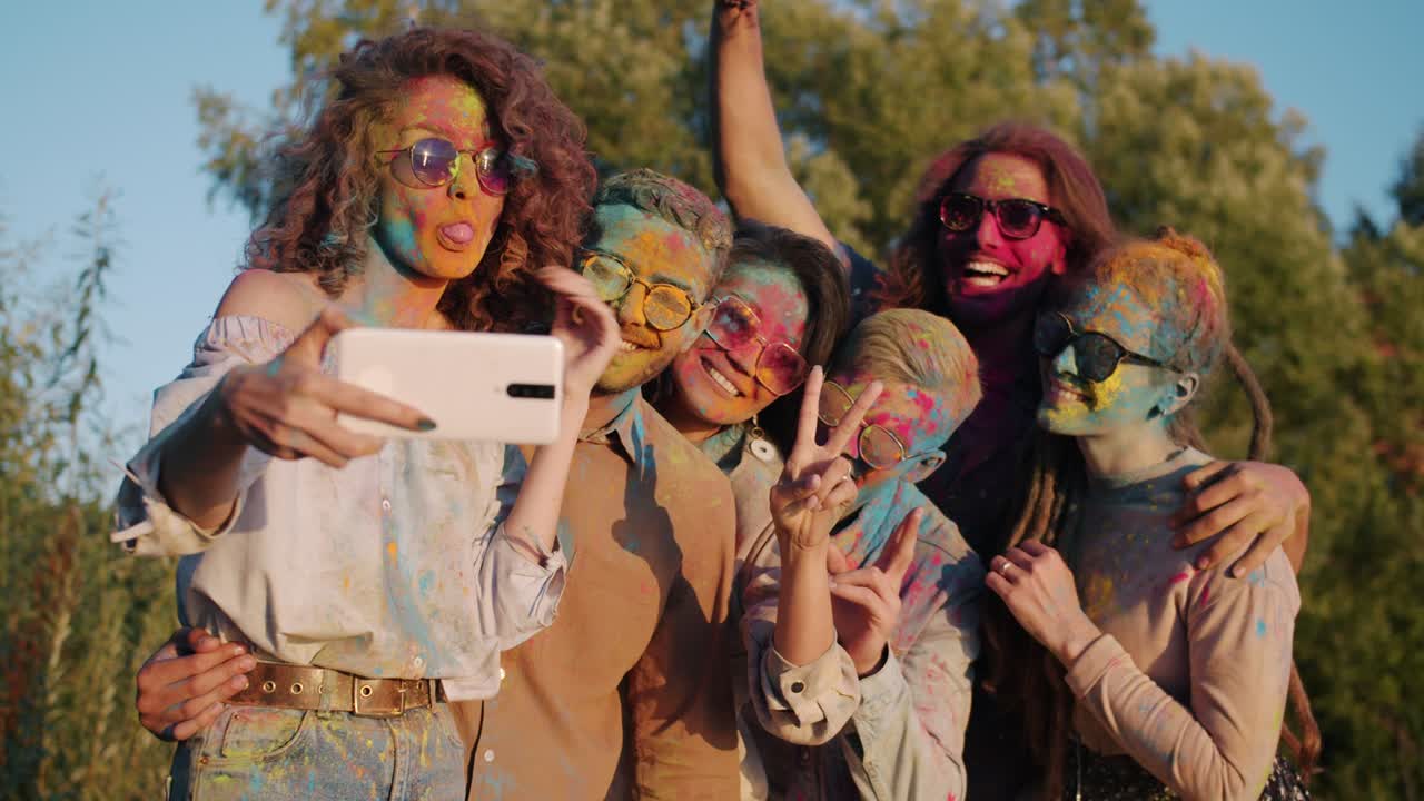 jóvenes felices tomando selfies con la cámara de su teléfono inteligente posando con caras pintadas durante la celebración de holi