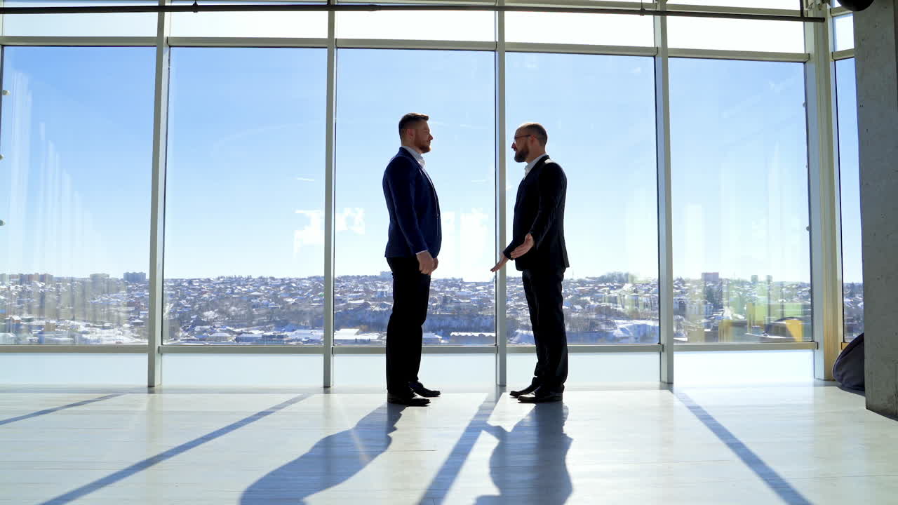 Businessman greeting in office. Top managers in business suits, shaking hands with each other, against the panoramic window view with a city background.