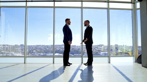 businessman greeting in office. top managers in business suits, shaking hands with each other, against the panoramic window view with a city background.