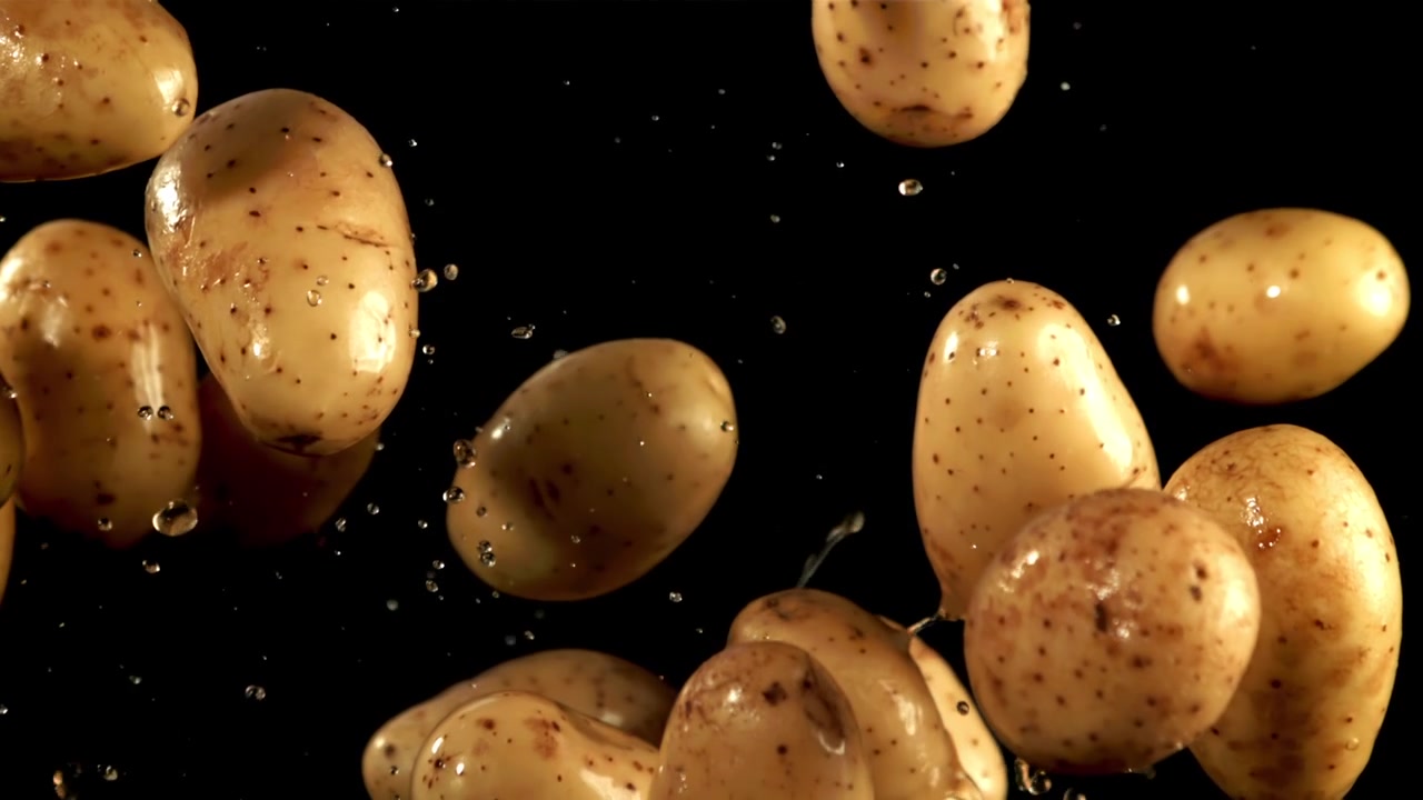 Patate biologiche fresche che cadono al rallentatore con goccioline d'acqua