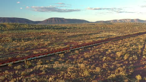 Excelente-Toma-Aérea-De-Un-Tren-De-Carbón-Que-Pasa-Por-Arbustos-Y-Montañas-En-Tom-Price,-Australia