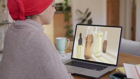 mujer biracial en la mesa usando portátil, compras en línea de productos de belleza, cámara lenta