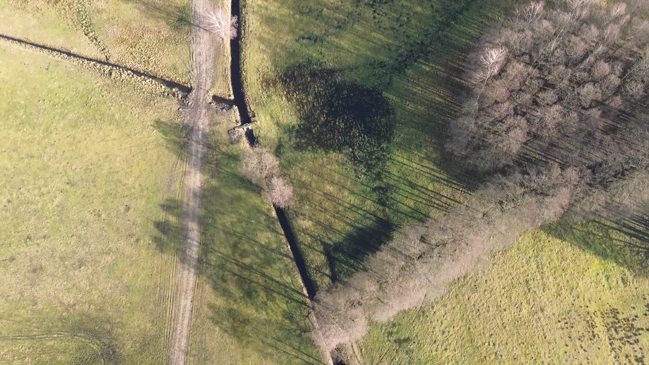 pov de pájaros en el camino de tierra y arroyo dirigiéndose a la granja con el ángulo aéreo alto de la vaca