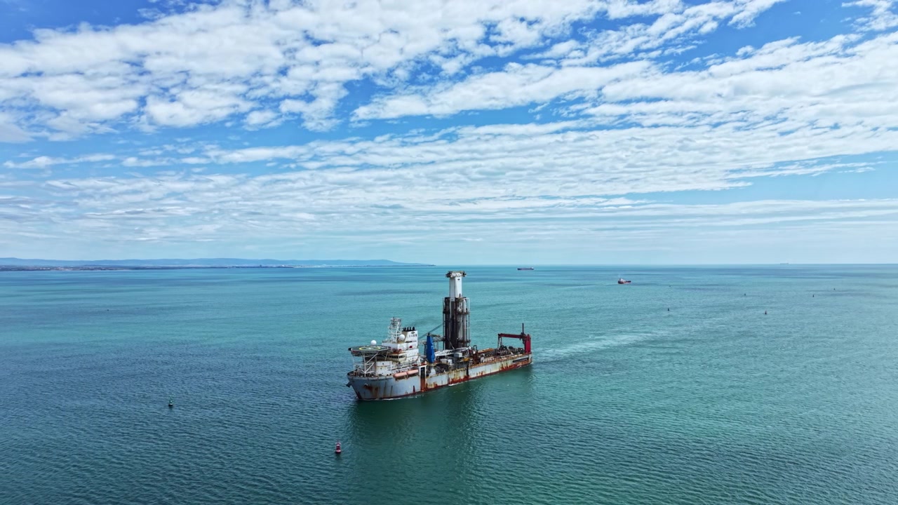 Industrial dredging vessel operates in the water with clear skies above and distant land visible in the background during the day