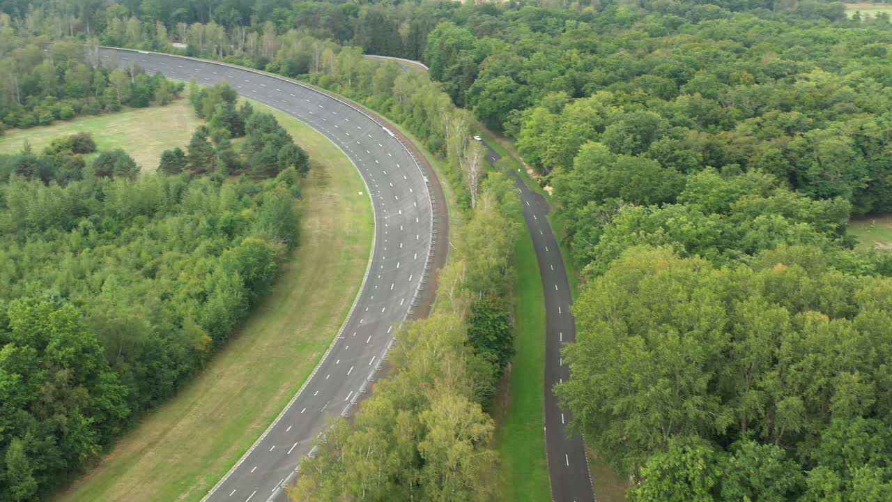 Aerial view of curving UTAC Mortefontaine race track through lush green forest, France