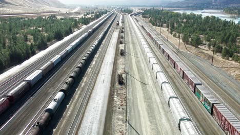 forward flight dolly wide drone shot flying over a railroad station in a desert environment on a sunny day next to a highway and a river and mountains in the background and powerines in the picture