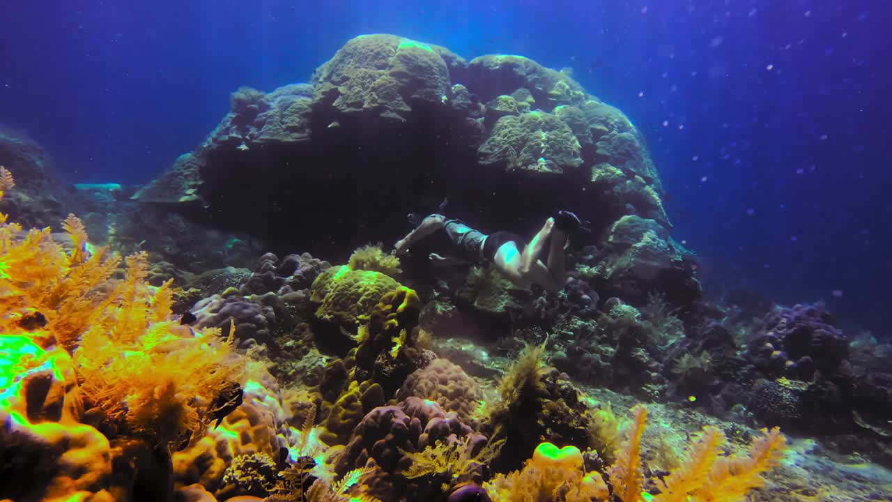 Penyelam snorkel berenang di dekat batu besar dan ganggang di laut biru, Bali, Indonesia