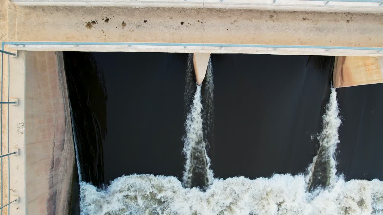 Top-down drone view of water gushing through dam spillway gates into the river channel. Pakistan