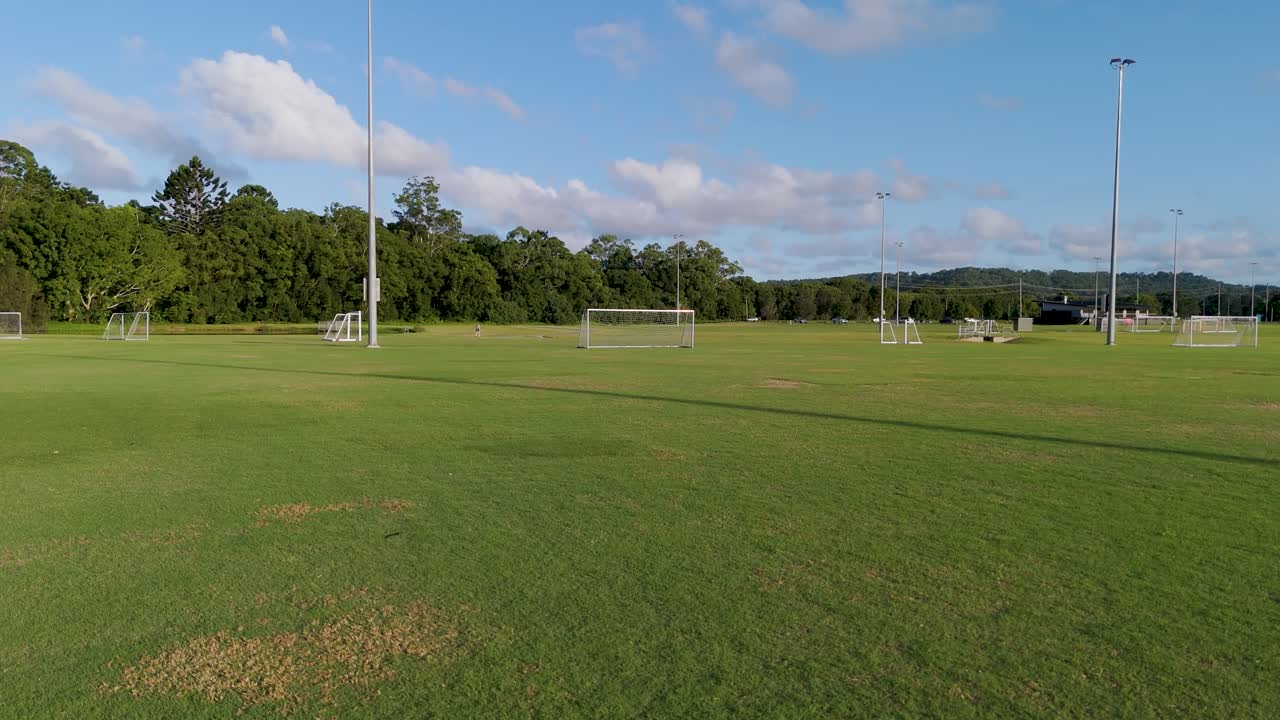 Aerial footage of a soccer field under clear skies, showcasing goalposts and lush greenery