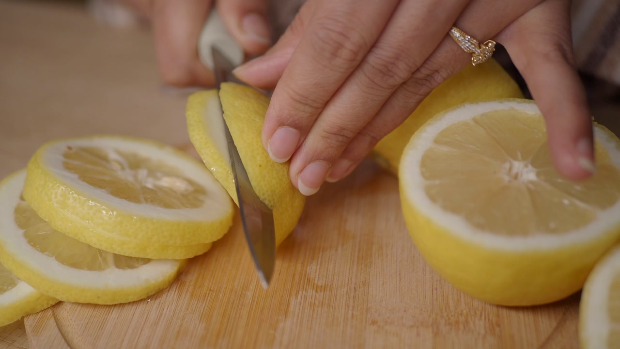 Close-Up of Hands Slicing Fresh Lemons on a Wooden Cutting Board