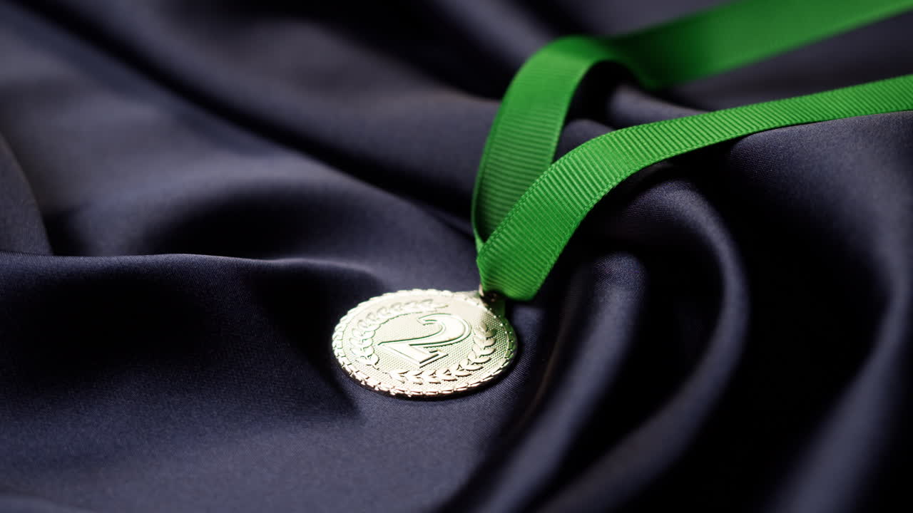 Silver Medal with Green Ribbon Displayed on Dark Fabric