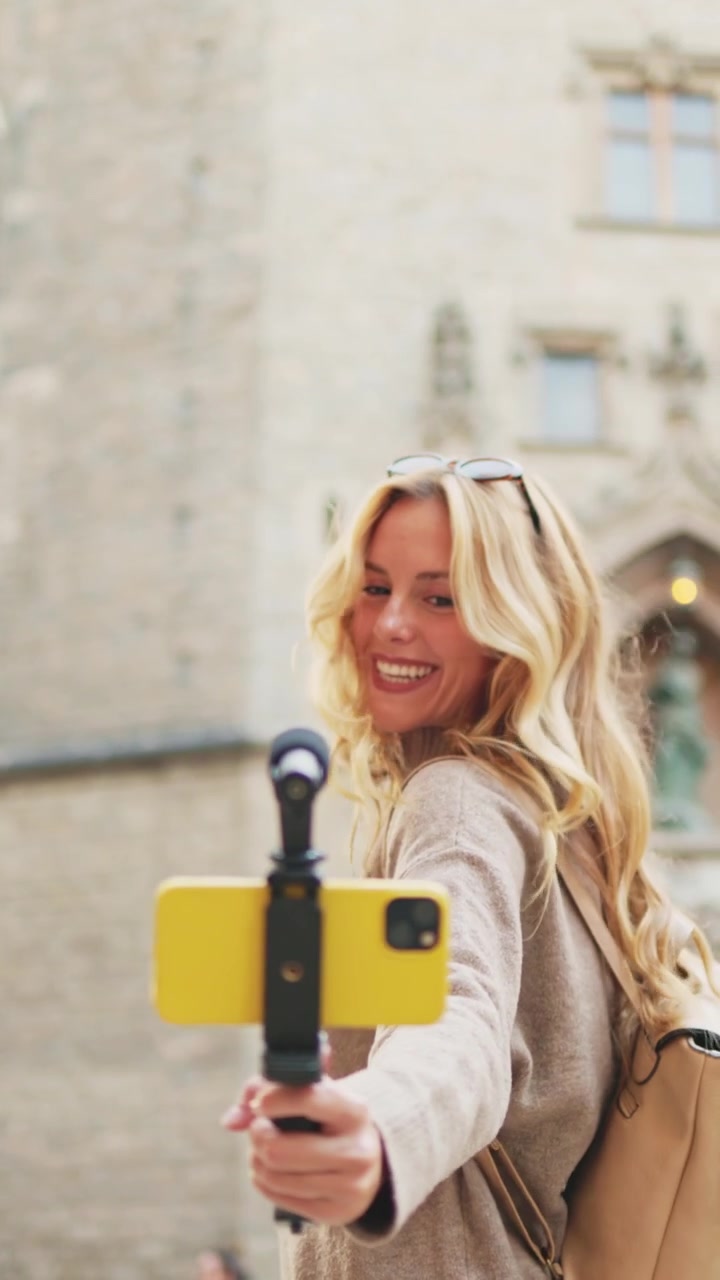 Giovane donna bionda che fa vlogging con lo smartphone per strada in città