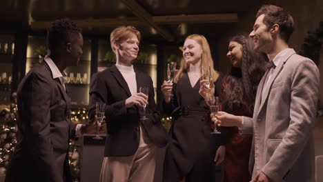 group of friends wearing elegant clothes toasting with champagne glasses and taking a sip in new year's party