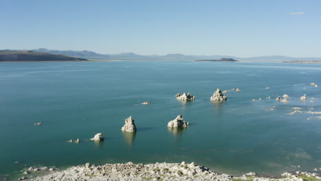 Vista-Aérea-Del-Lago-Mono-Con-Sus-Distintivas-Formaciones-De-Toba-Que-Se-Elevan-Desde-El-Agua,-Rodeado-Por-Un-Vasto-Y-Sereno-Paisaje-Bajo-Un-Cielo-Azul-Claro