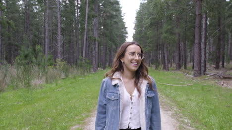 mujer joven caminando y riendo a lo largo del sendero en un exuberante bosque verde