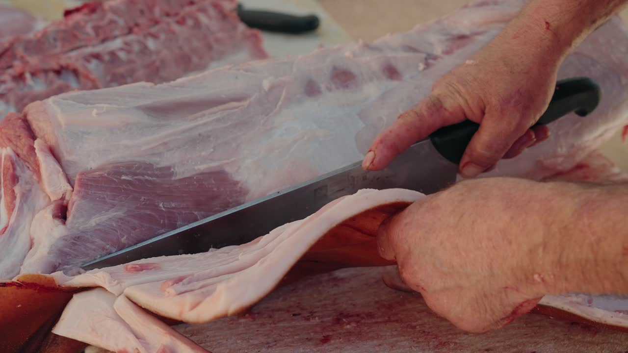 hands cut through pork slab using large cleaver with steady grip